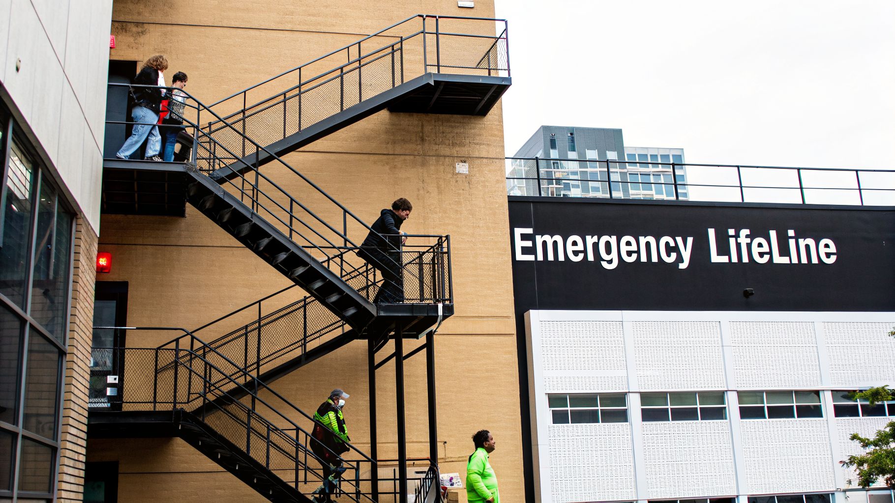 People walk up and down a black metal fire escape on a tan building next to a sign.