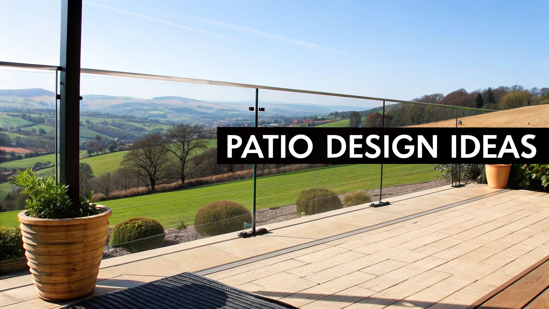 A modern patio with a glass railing overlooking a lush green valley and rolling hills.