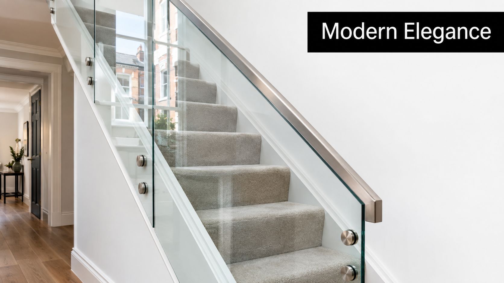 A modern staircase featuring clear glass balustrades with metal mounts and soft grey carpeted steps.